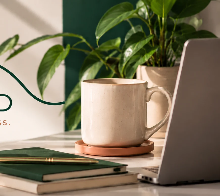 Warm contemporary workspace with a coffee cup, notebooks, greenery and laptop